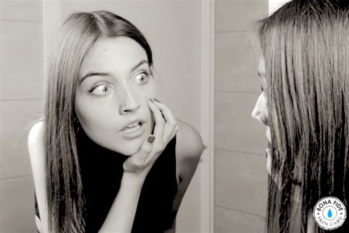 Girl looking at recurring pimple in mirror